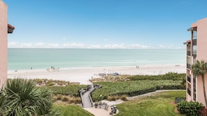 A beachfront hotel with a clear view of the ocean, a patio area with seating, and a pathway leading to the beach. - Beachfront Condo on Famous Siesta Key! (Sarasota)