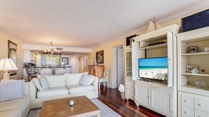 A living room with a white sofa, a coffee table, and a TV displaying a beach scene. - Beachfront Condo on Famous Siesta Key! (Sarasota)