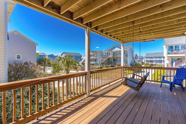 A wooden deck with a swing chair and a blue chair, overlooking a residential area with multi-story buildings.
