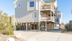 A two-story beachfront house with a balcony and a covered porch.