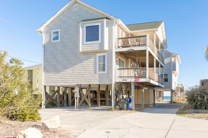 A two-story beachfront house with a balcony and a covered porch.