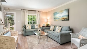Ein Wohnzimmer mit zwei grauen Sofas, einem Glastisch und einem Korbsessel.