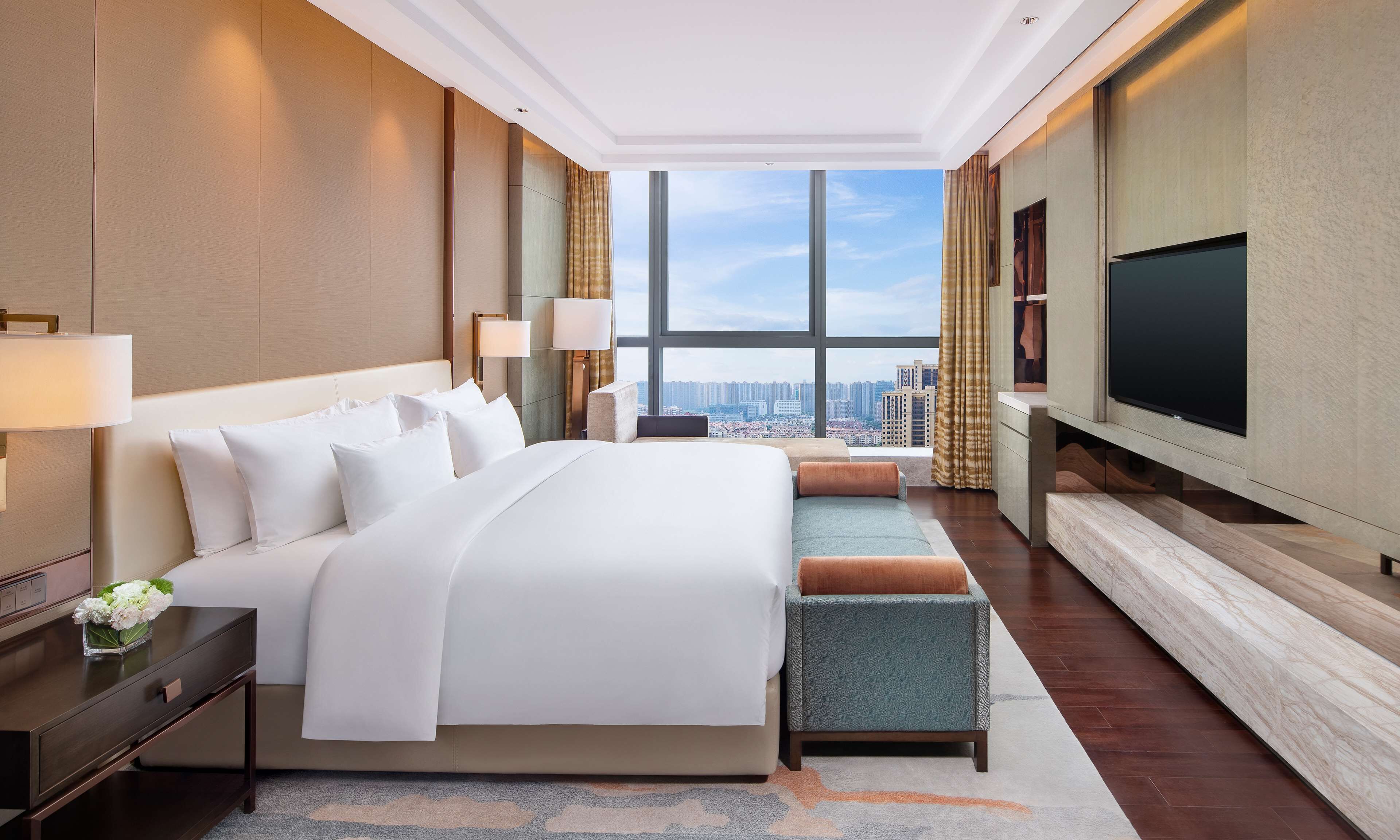 Una habitación de hotel moderna con una cama grande, televisión y vistas a la ciudad.