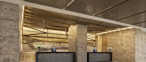A modern lobby with two reception desks, a high ceiling with exposed beams, and a marble floor.