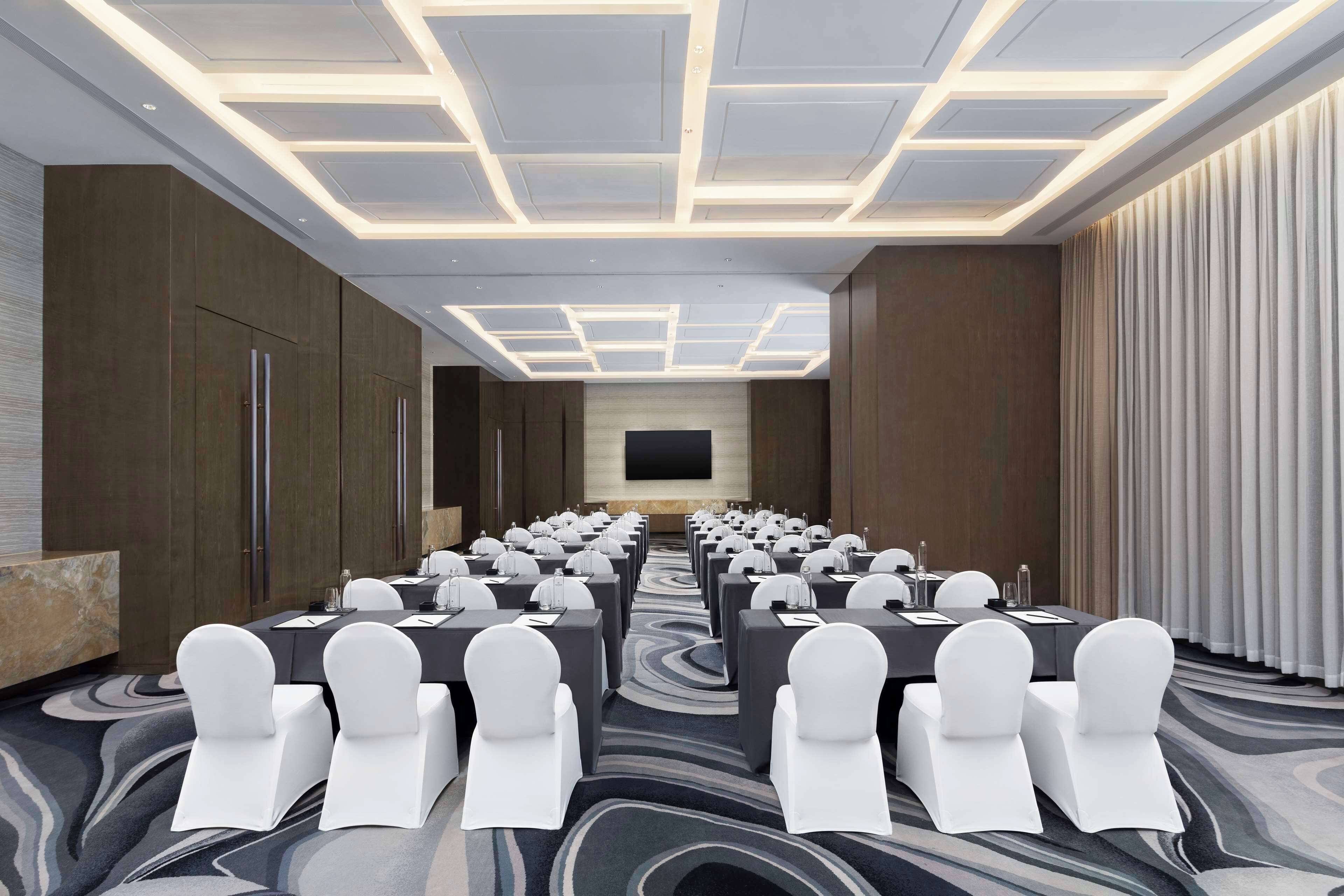 Un salón de conferencias con una larga mesa, sillas blancas y un diseño de techo moderno.