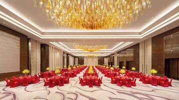 A spacious banquet hall with rows of round tables, red chairs, and a central chandelier.
