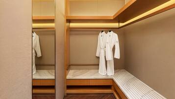 A modern, minimalist bathroom with wooden flooring, a bench, and two white robes hanging on hooks.