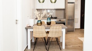 Eine moderne Küche mit weißen Schränken, einem Edelstahlkühlschrank und zwei Korbstühlen an einer weißen Kücheninsel.