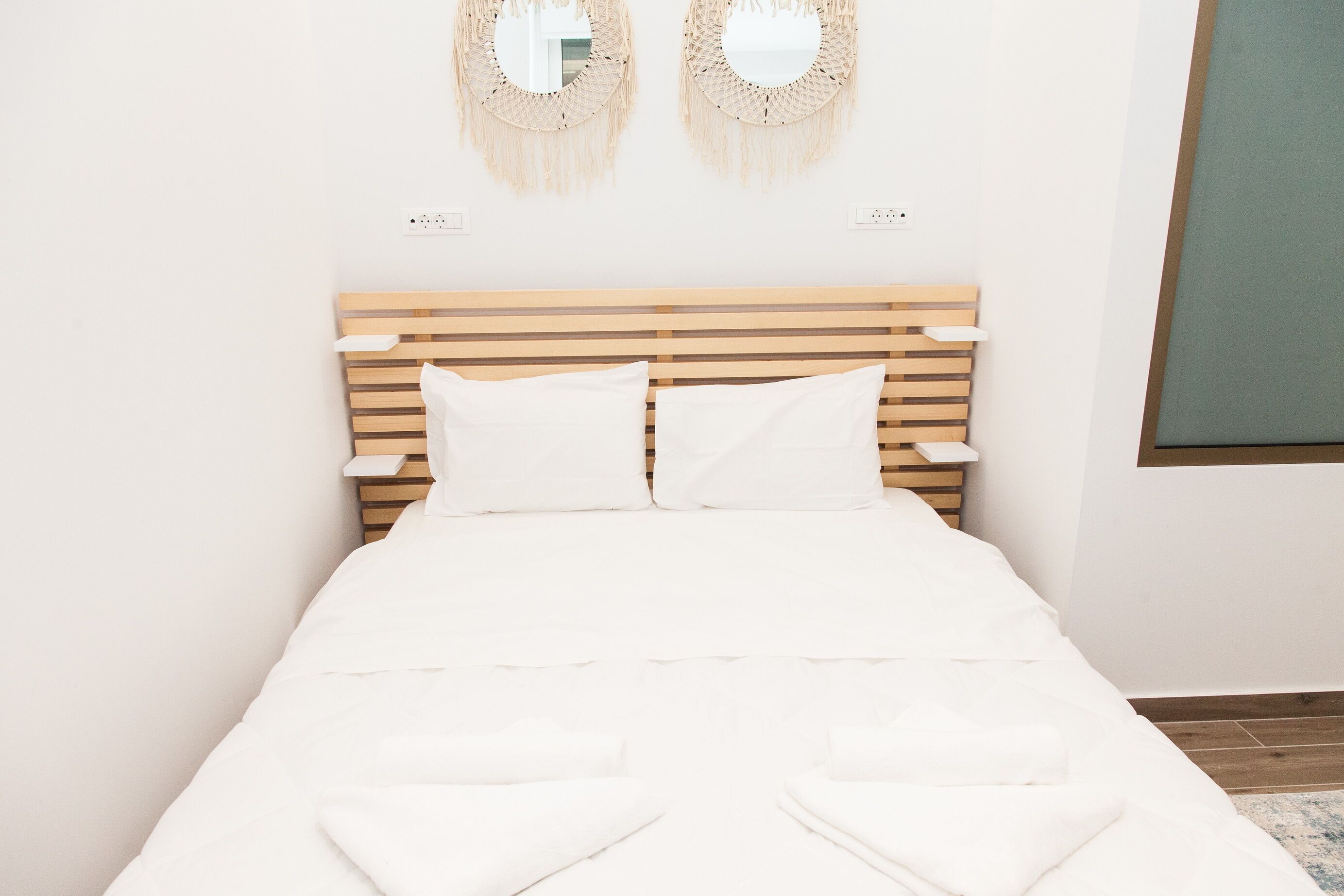 A neatly made bed with white linens and a wooden headboard. There are two wall-mounted decorative mirrors above the bed.