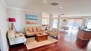 A spacious living area with a sofa, armchairs, a coffee table, and a painting of a beach scene. - Wagon Holiday Home - modern home in great Abbey location! (BROADWATER)
