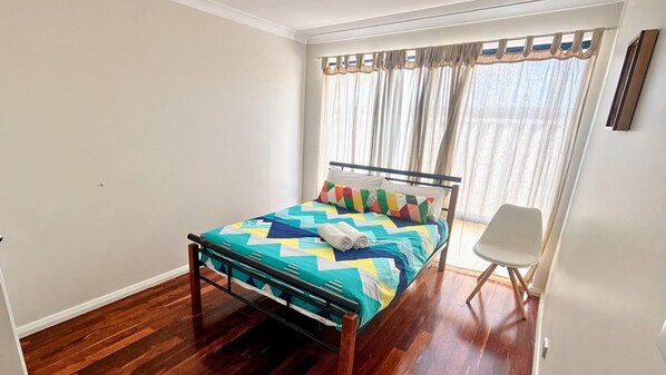 Uma cama de solteiro com um edredom colorido, uma cadeira e uma janela com cortinas.