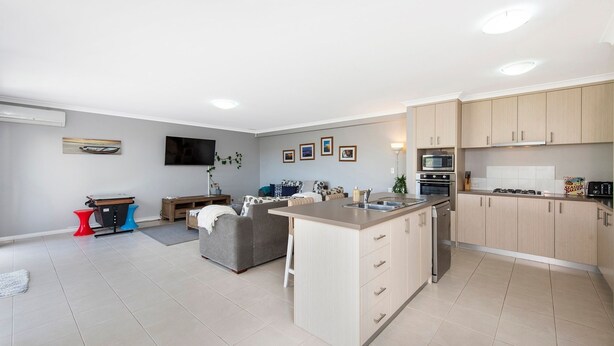 Een moderne keuken met een centraal eiland, ingebouwde apparatuur, en een zithoek met een grijze bank en een rode accentkruk.