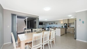 Een moderne keuken met een centraal eiland, een eethoek met een houten tafel en witte stoelen, en een zithoek met een bank en televisie.
