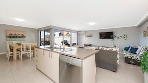 Een moderne keuken met een vaatwasser, een eethoek met stoelen, een bank en een aan de muur bevestigde televisie.