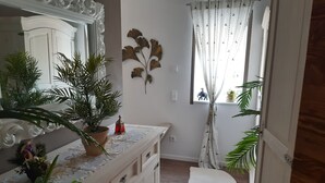 A room with a large mirror, a dresser with drawers, a potted plant, a decorative wall piece, and a window with curtains. - Chic apartment (Altershausen/Münchsteinach)