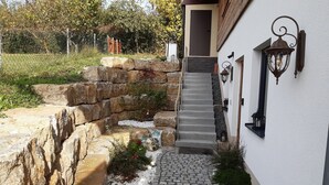 A stone staircase leading to a door, surrounded by a white wall with a lantern and a small garden area with white pebbles and plants. - Chic apartment (Altershausen/Münchsteinach)