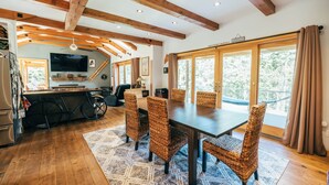 A spacious dining area with a wooden table and wicker chairs, a kitchen with a refrigerator and a television, and large windows offering a view of the outdoors. - Coastal Waterfront Retreat with Sauna, Kayaks & Fire Pit, Freeport, Near LL Bean (Freeport)