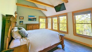 A bedroom with a large bed, wooden beams, a flat-screen TV, and large windows. - Coastal Waterfront Retreat with Sauna, Kayaks & Fire Pit, Freeport, Near LL Bean (Freeport)