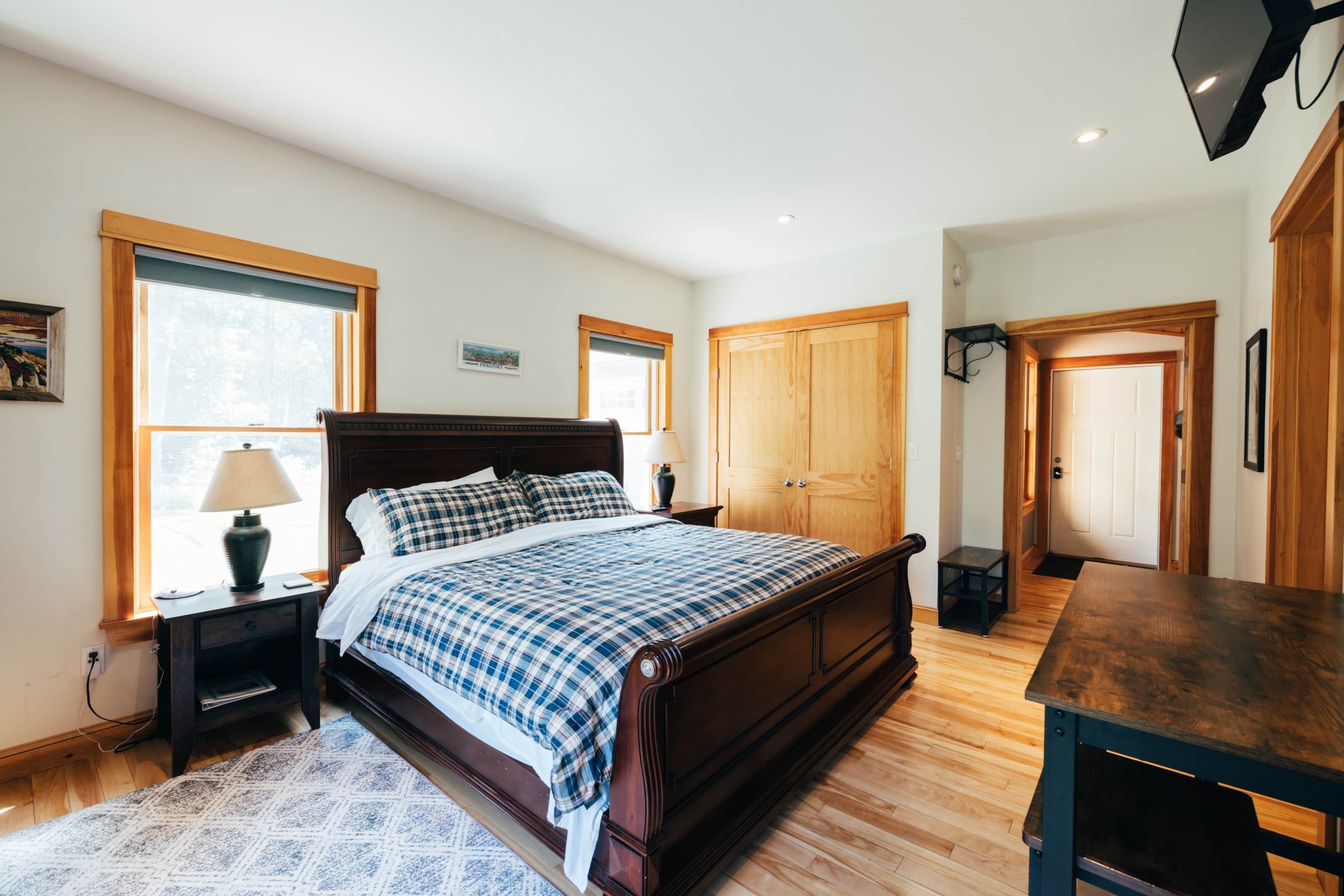 A bedroom with a wooden bed, two bedside tables, a nightstand, a wooden desk, and a door.