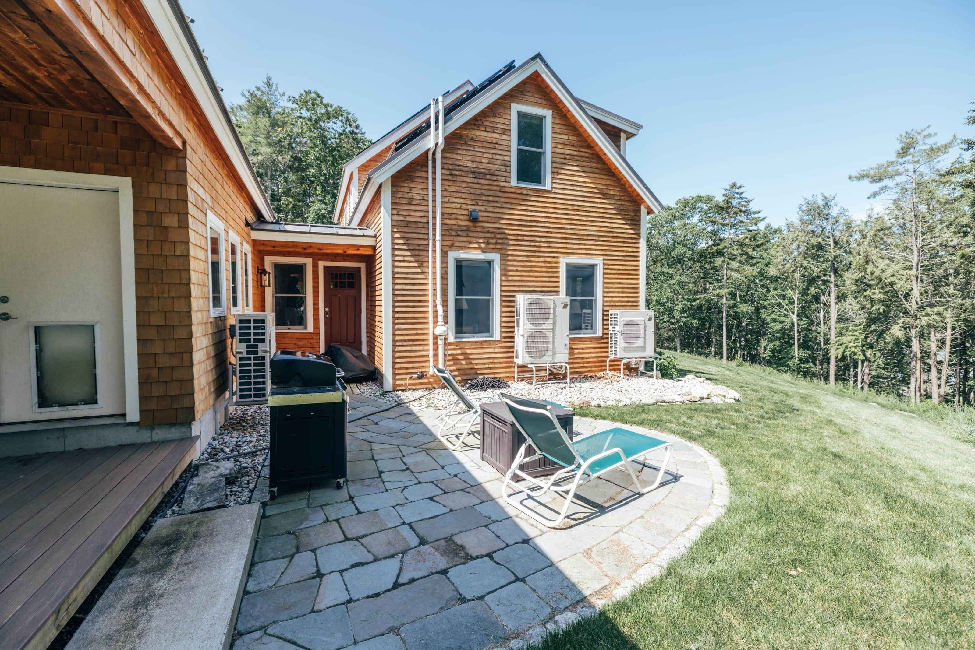Une maison en bois avec un patio en pierre, un espace salon extérieur et un garage.