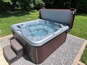 A hot tub with a wooden frame and a built-in seat, placed on a gravel surface in a grassy area. - Sunday River Chalet w/ Hot Tub, Fire Pit & River Access Near Ski Lifts (Bethel)