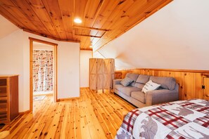 A room with wooden flooring, a sofa, a bed with a plaid cover, and a wooden wardrobe. - Sunday River Chalet w/ Hot Tub, Fire Pit & River Access Near Ski Lifts (Bethel)