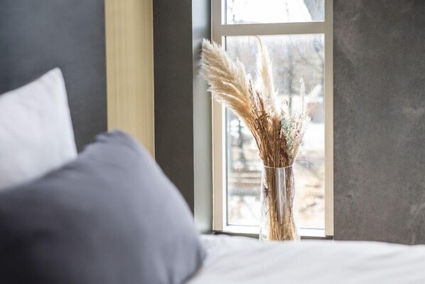 A bed with a white pillow and a vase with dried plants by a window. - Peak 12 Hotel (Viborg)