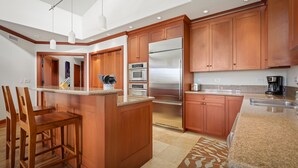 A modern kitchen with wooden cabinets, stainless steel appliances, and a granite countertop. - Hale Inu Waina: Spacious 2BR condo in Waikoloa with scenic views. (Waikoaloa)
