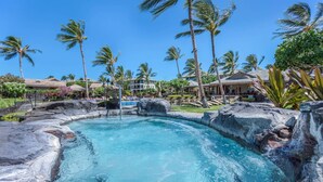 A pool with a rocky edge, surrounded by palm trees and lounge chairs. - Hale Inu Waina: Spacious 2BR condo in Waikoloa with scenic views. (Waikoaloa)
