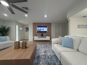 Ein modernes Wohnzimmer mit einem Flachbildfernseher, weißen Sofas, einem Couchtisch und einem gemusterten Teppich.