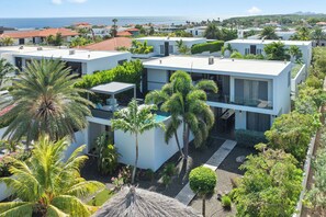 A modern residential complex with multiple white buildings, a swimming pool, and lush greenery.