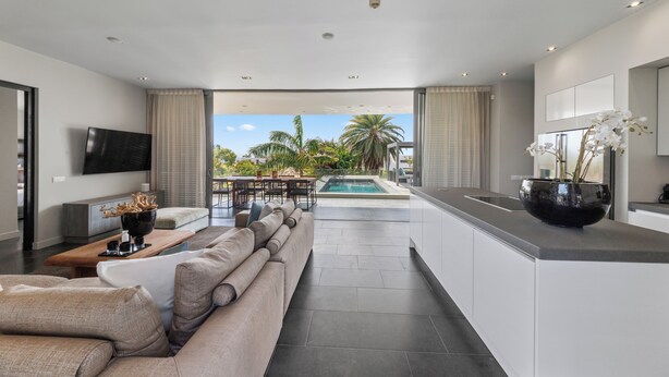 Una cocina moderna con una isla grande, un comedor con vistas a la piscina y un salón con sofá y televisor.