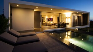 Una casa moderna con piscina exterior, comedor y sala de estar con televisor.