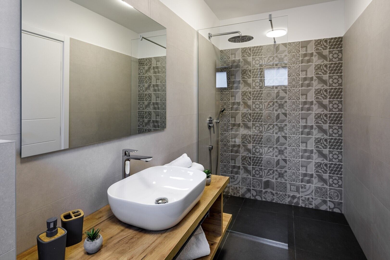 Een moderne badkamer met een vrijstaand bad, een douche met glazen wanden en patroon betegelde muren.