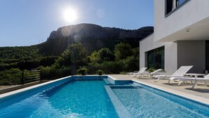 Ein Swimmingpool mit Bergblick, umgeben von einem modernen Gebäude mit Liegestühlen.