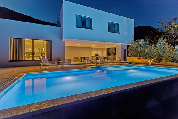 Um edifício moderno de dois andares com piscina, área de estar externa e interior bem iluminado.