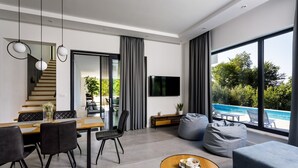Ein modernes Wohnzimmer mit Essbereich, einem an der Wand montierten Fernseher und Blick auf einen Swimmingpool.