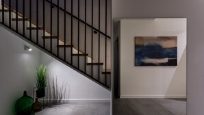 Eine moderne Treppe mit schwarzer Geländer und Holzboden, die zu einem Raum führt, in dem ein großes, abstraktes Gemälde an der Wand hängt.