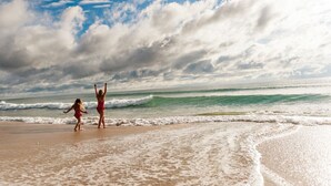 Escena de playa con dos personas caminando por la orilla.