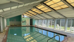 Una piscina interior con paredes de vidrio transparente, suelo de baldosas y techo con tragaluces.
