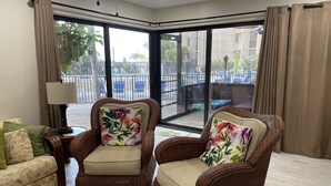 Une pièce d’angle avec des fauteuils en osier, une lampe et une vue sur un balcon aménagé avec du mobilier d’extérieur.