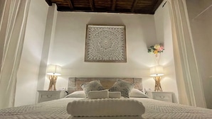 Een net opgemaakt bed met een witte deken en twee kussens, met nachtkastjes en lampen aan weerszijden, en een decoratief kunstwerk erboven.