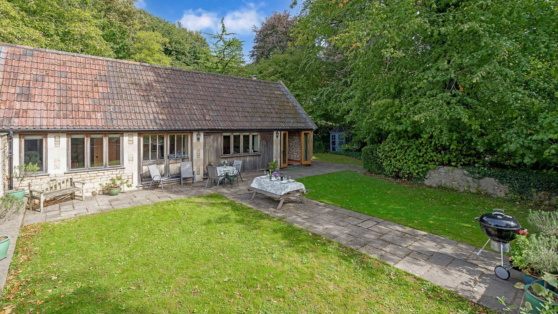 Une maison de campagne au toit en tuiles, dotée d’un patio avec des meubles d’extérieur et d’un barbecue.