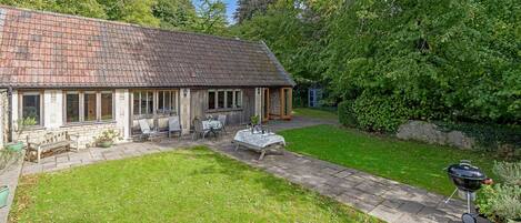 Une maison de campagne au toit en tuiles, dotée d’un patio avec des meubles d’extérieur et d’un barbecue.