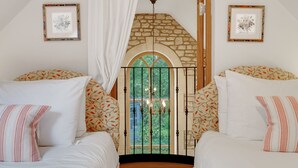 Un dormitorio con dos camas, una pared de piedra, una ventana con vistas y cuadros enmarcados en las paredes.