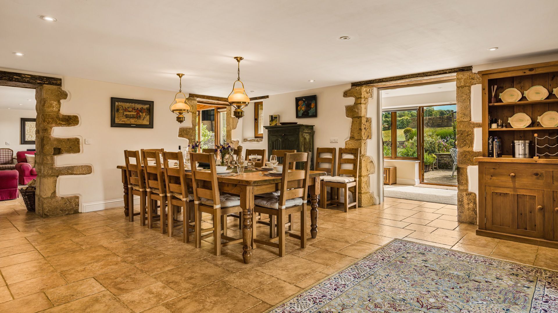 A dining area with a wooden table and chairs, stone pillars, and a view of the garden through a glass door.