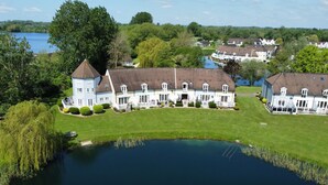 A large, multi-story building with a central tower, surrounded by a well-maintained lawn and a body of water. - Mayfly Lodge - sleeps 6 guests  in 3 bedrooms (Cotswold Lakes)