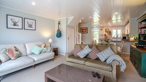 A cozy living room with a sofa, a coffee table, and a dining area with a kitchen in the background. - Mayfly Lodge - sleeps 6 guests  in 3 bedrooms (Cotswold Lakes)