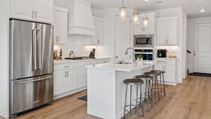 Une cuisine moderne avec des meubles blancs, des appareils en acier inoxydable et un îlot central doté de tabourets de bar.