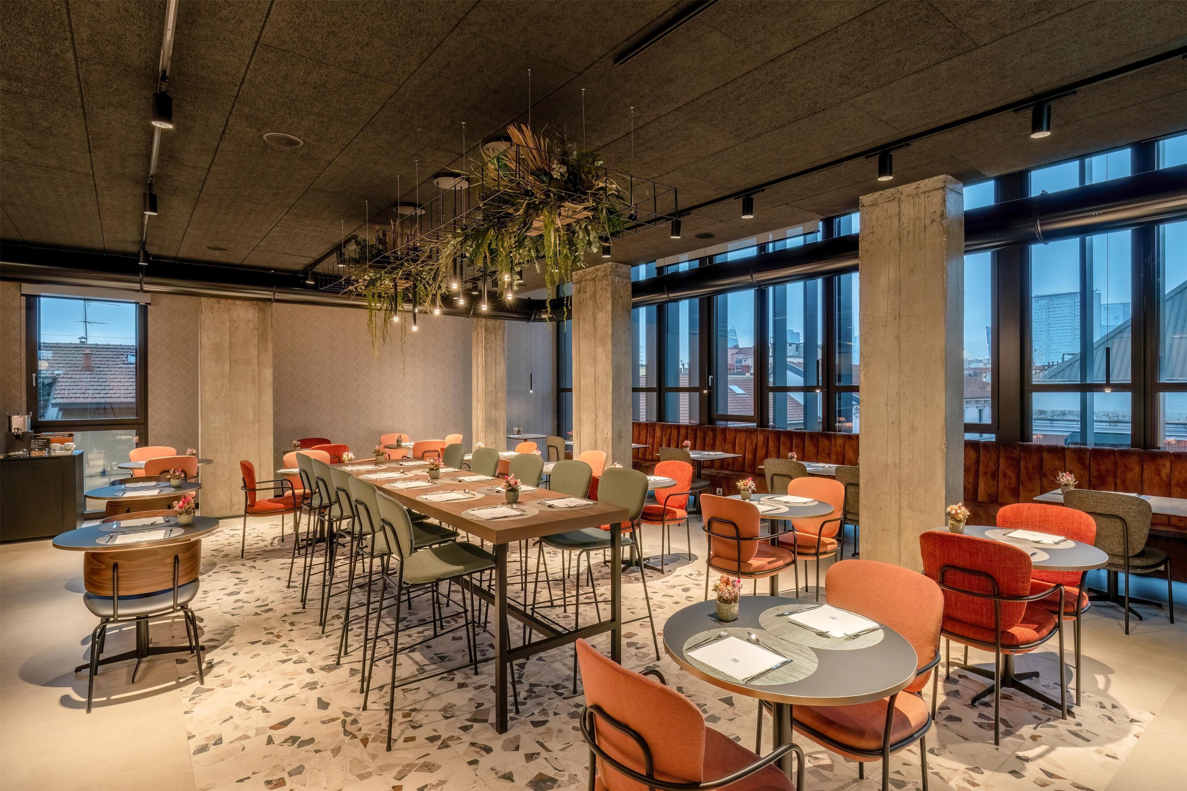 Un comedor moderno con techos altos, ventanas grandes y una combinación de mesas redondas y rectangulares.